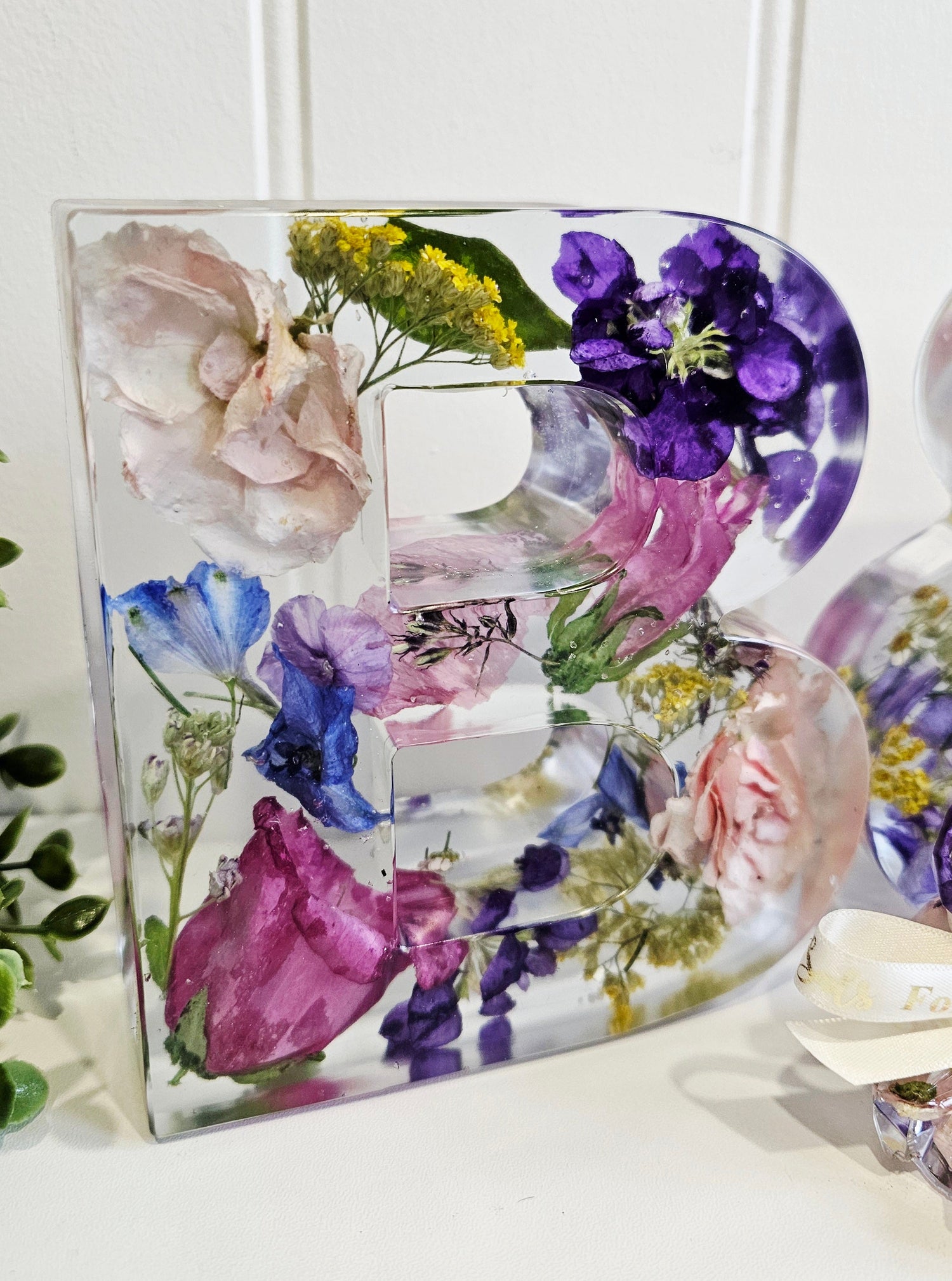 Decorative letter 'B' made of pressed flowers on a white background