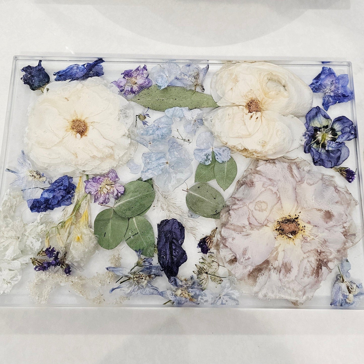 Decorative glass tray with pressed flowers on a white surface