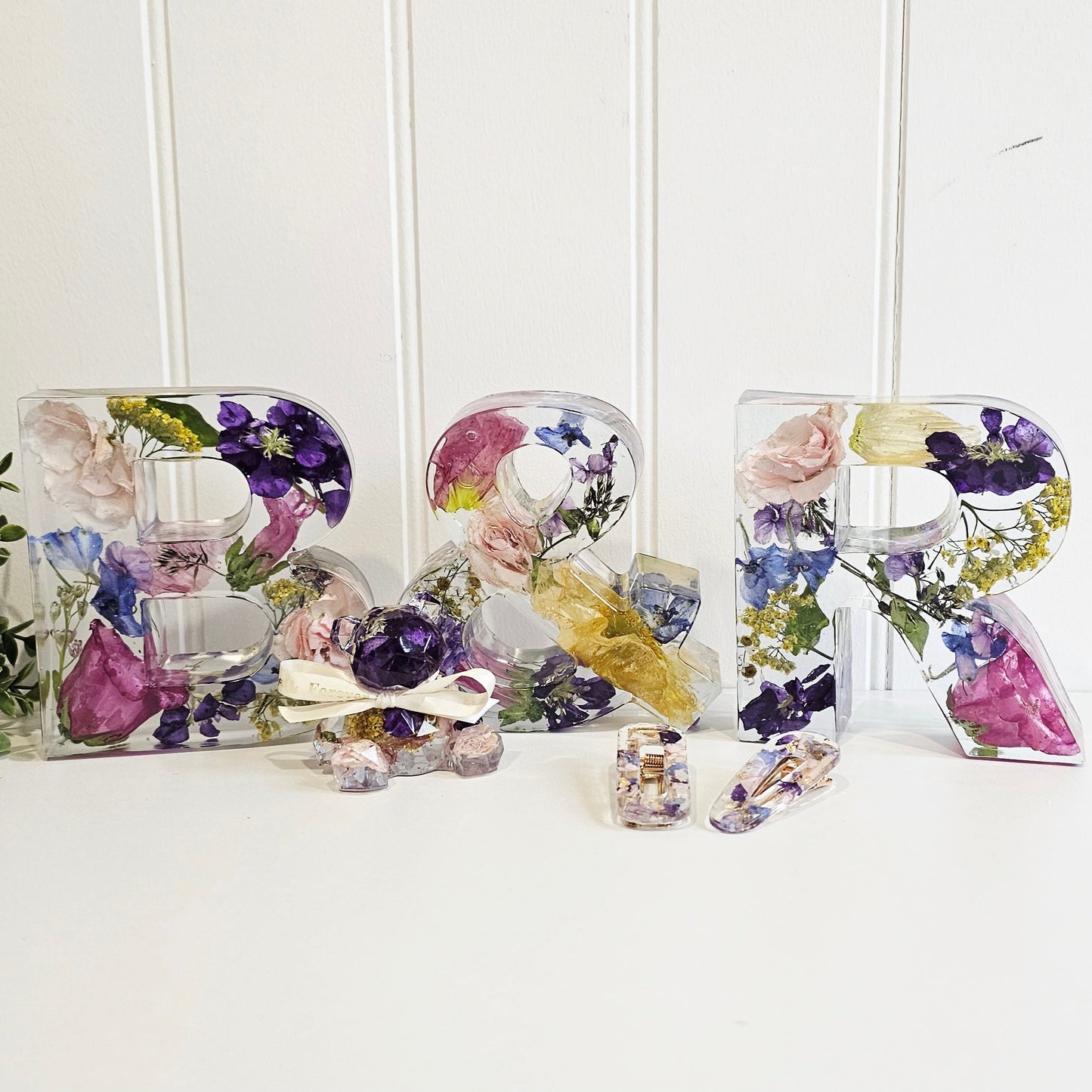 Decorative letters made of resin and pressed flowers on a white surface with a white background.