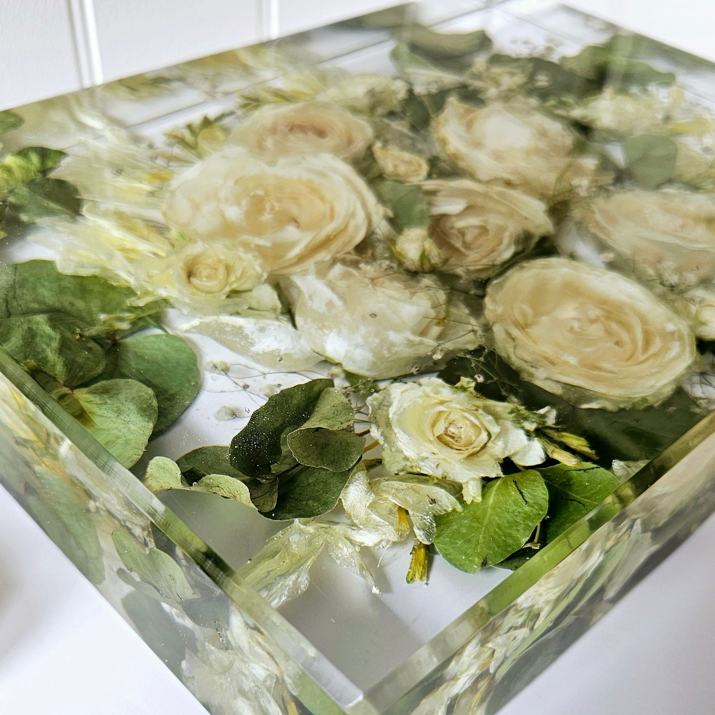 Decorative resin block preserved flowers and greenery on a white surface