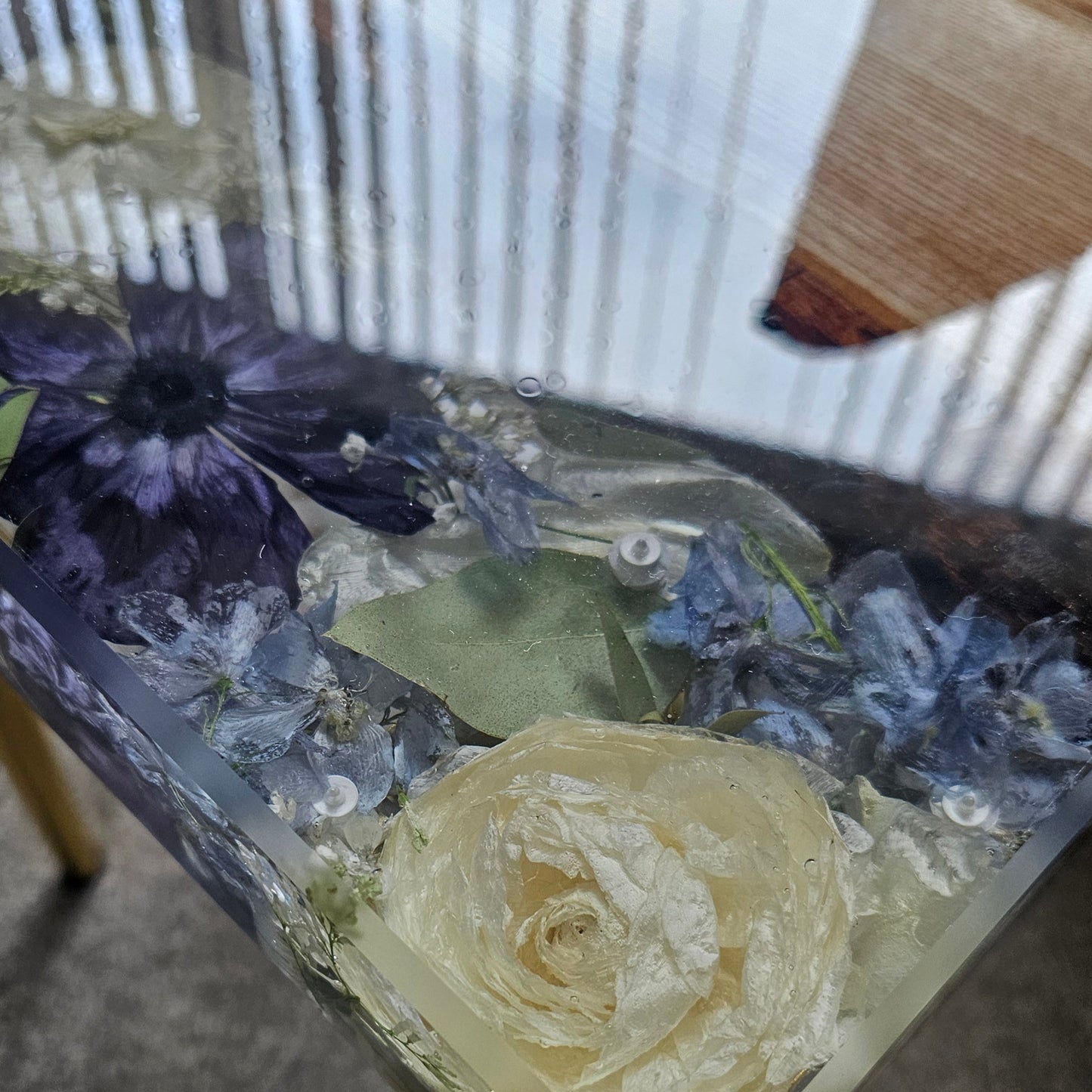 Decorative table with a rose and purple flowers embedded in a clear resin material, placed on a textured surface.