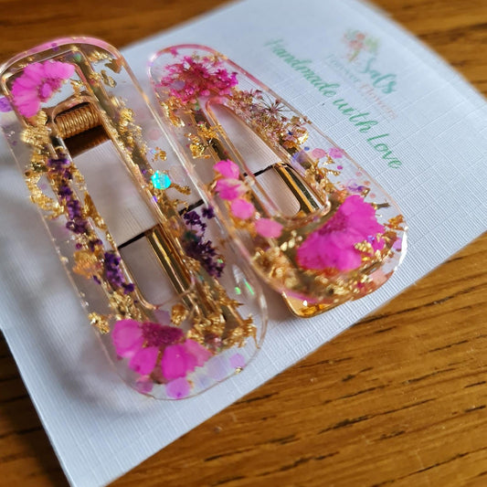 Decorative hair clips with pink flowers and gold accents on a white card.