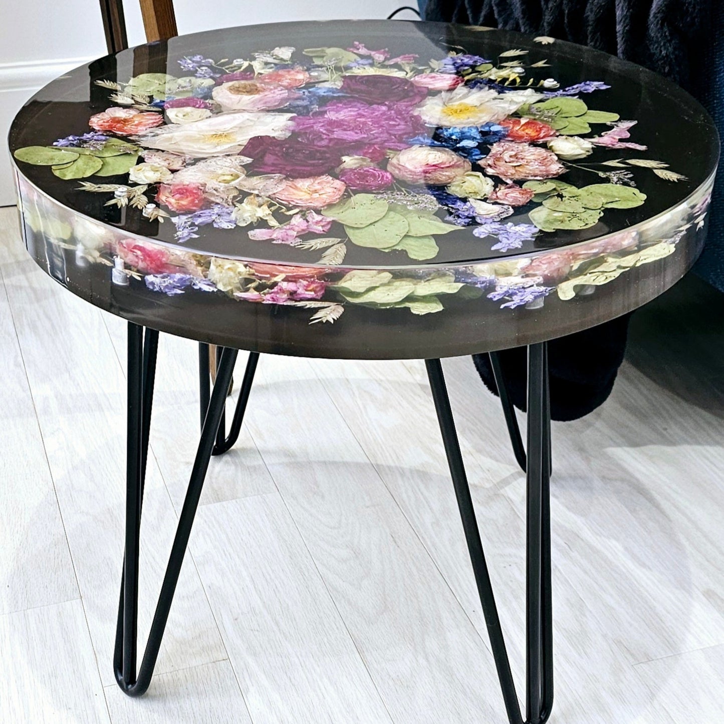 Round resin side table with floral design on a white floor next to a blue chair.