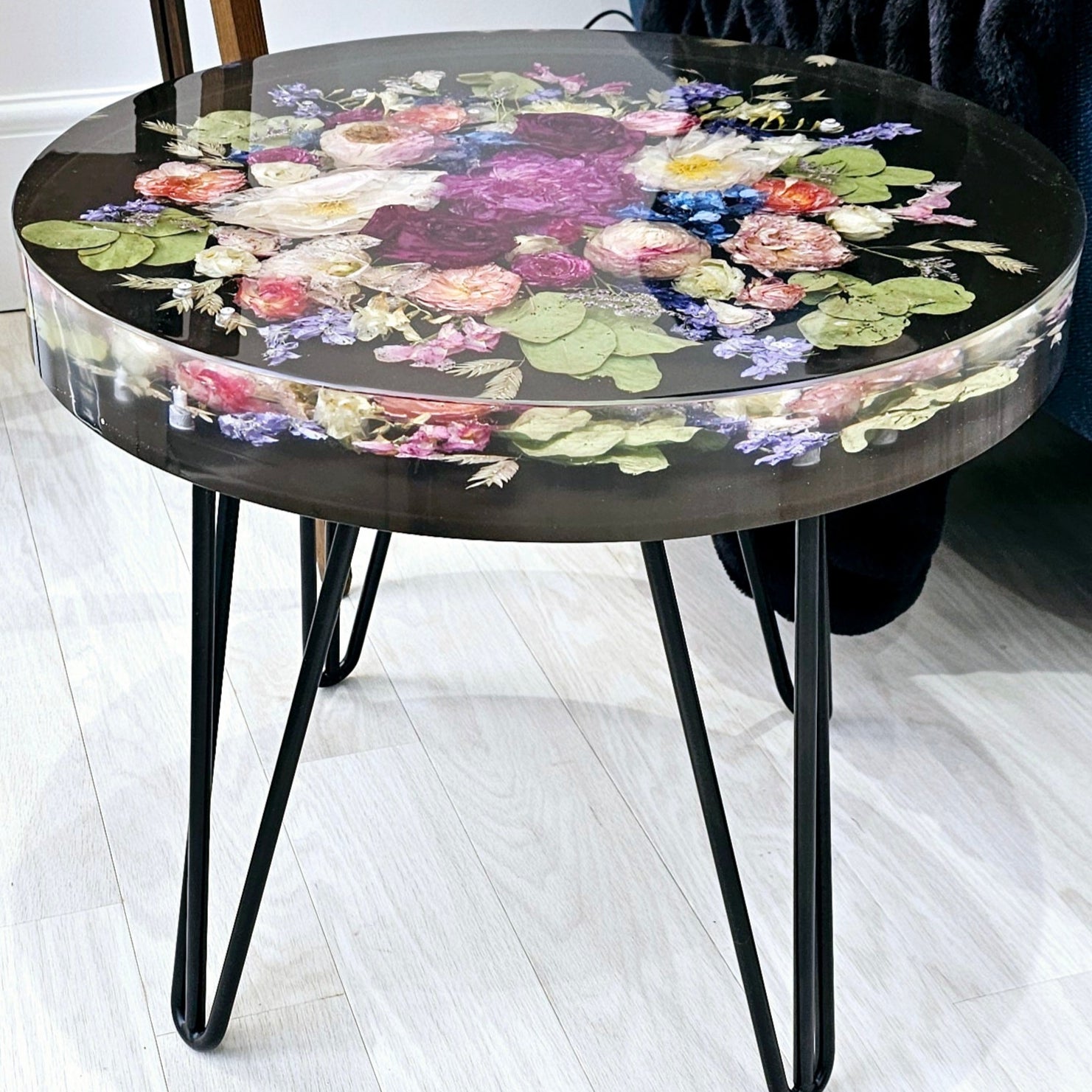 Round resin side table with floral design on a white floor next to a blue chair.