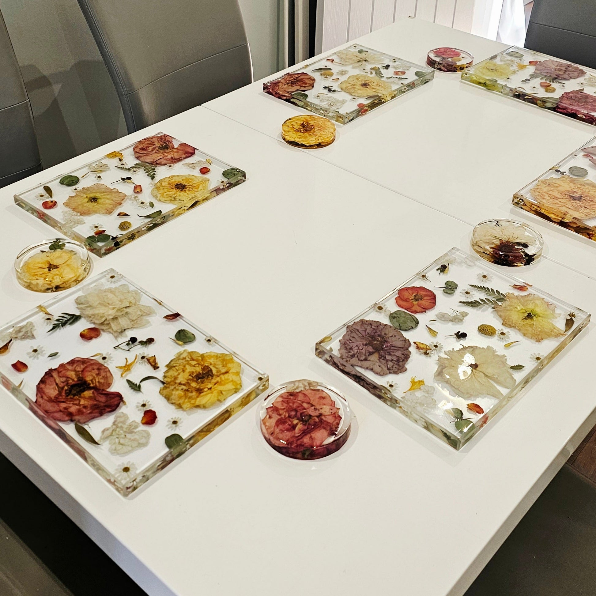Dining table with floral resin placemats and plates in a room with chairs and a window.