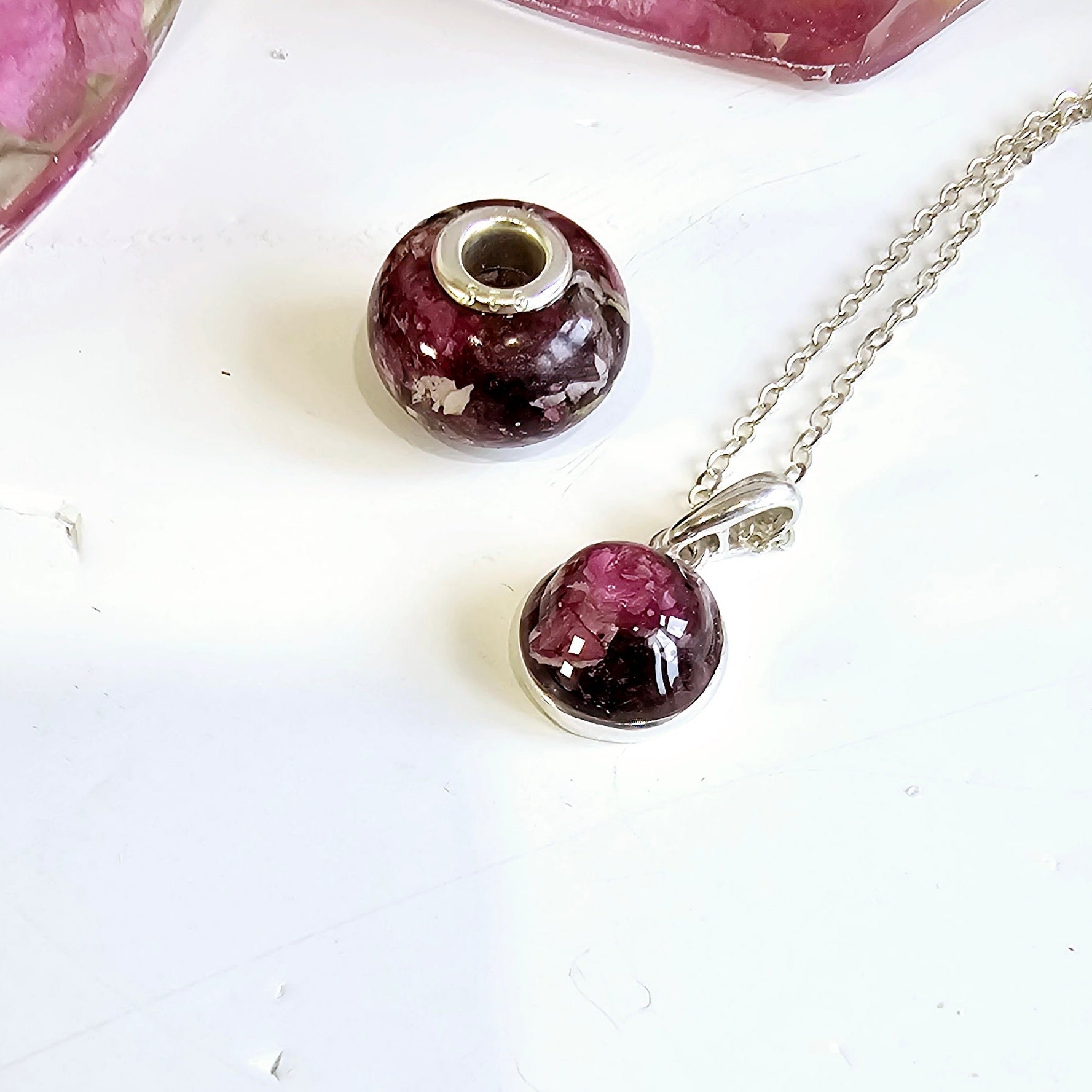 Necklace with a purple pendant  and pandora style bead charm on a white surface. made with flowers in resin